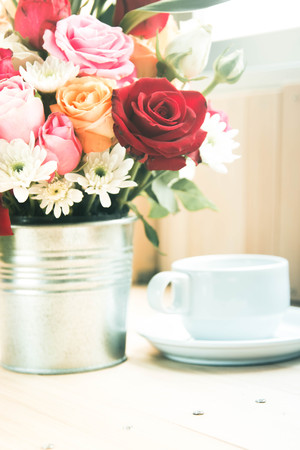 Vase of bouquet Roses in aluminium bucket and white cup of coffee on wooden table, set of Beautiful flowerの写真素材