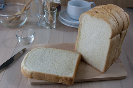 Pile of Slice Fresh fragrant bread on chopping block. coffee cup and kitchen ware put on wooden...