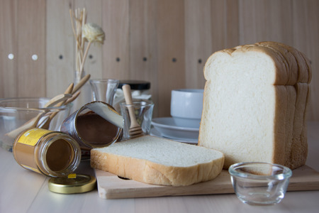 Slice bread with peanut butter and chocolate sweet bottle put on wooden table with kitchen ware and bowl glass.の写真素材