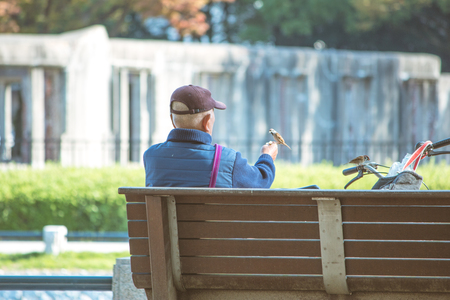 senior man sit alone at bench in park, at Atomic Dome from Hiroshima Peace Memorial park in the autumn season of Hiroshima, Japan.の写真素材