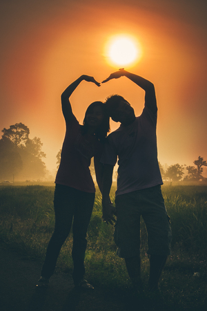 Silhouette of lovely couple against sunset. blow arm to heart shape, Love and romance concept.の写真素材