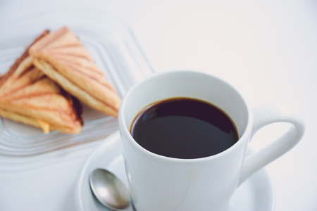 White cup of hot black coffee with morning fresh croissant on white table. smoke and scented arabica coffee bean in fresh morningの写真素材