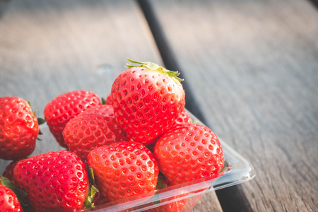Close up pile of fresh strawberry in plastic package put on wooden tableの写真素材