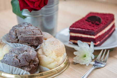 Custard and chocolate Chu cream and Red velvet cheese cake topping by dark chocolate on white plate and fork. Cup of coffee and vase of bouquet roses put on wooden table.の写真素材