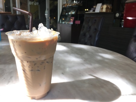 Plastic glass of ice latte coffee on wooden table bar near the window at cafe shop and restaurant.の素材