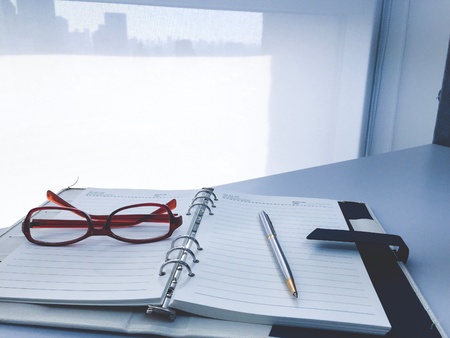 Pen on notebook and glasses on table in modern officeの素材