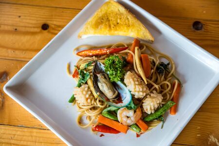 Seafood spaghetti, shrimp, squid, vegetables Asian cuisine is popular on white plates on wooden floors.の写真素材