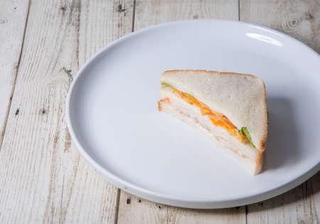 Sandwich with chicken and vegetables on a white plate on a wooden background
