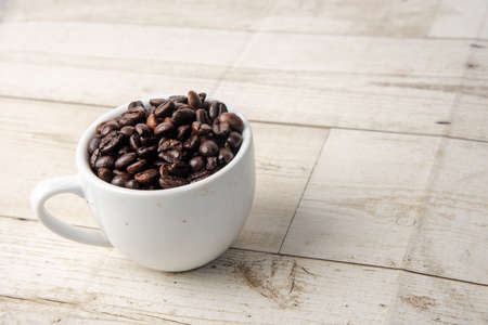 Arabica and Robusta roasted coffee beans in white glass on wooden background cutoutの写真素材