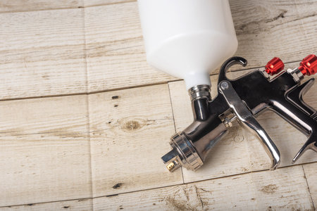 Paint spray on wooden floors Image of the painter's arm hand holding industrial size spray gun used...