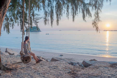 woman on a ocean beach swing that hangs with watching a sunrise or a sunsetの写真素材