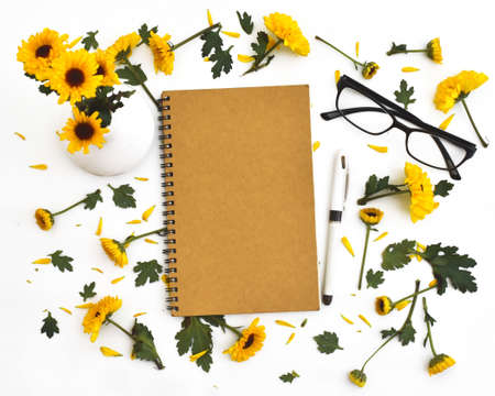 Framework from yellow flowers on white background. Flat lay composition with notebook pen and glassesの写真素材