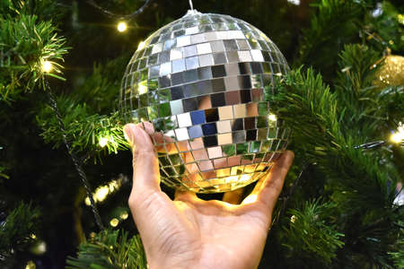 Mirrored shiny silver disco ball decorate hold by hand on christmas treeの写真素材