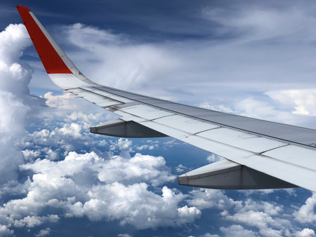 Airplane wing under beautiful cloudy sky visible from window