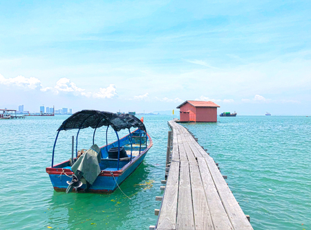 Wooden bridge at Clan Tan Jetty on a cloudy day with blue sky and fisherman boatの写真素材