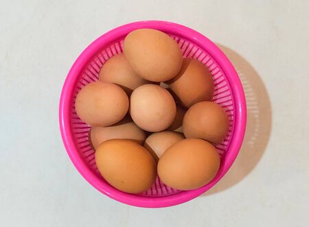 Chicken eggs in a pink plastic basket on white background.