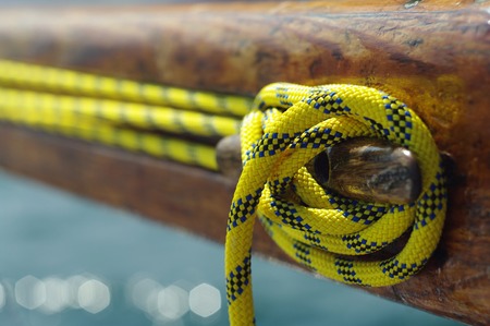 Closeup of old vintage snatch cleat with yellow line on wooden yacht, tool for keeping ropes...