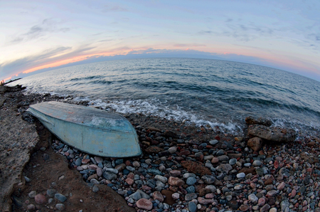Old boat at Issyk-Kul lake shore, sunset landscape with beautiful stones and surfの写真素材