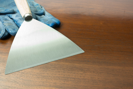 paint scraper with wood handle and working gloves.