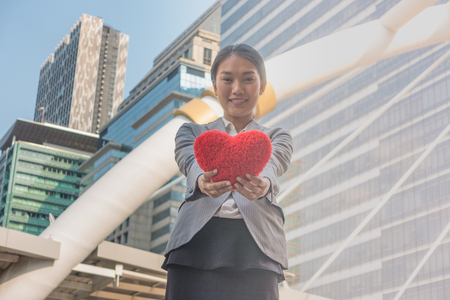 Beautiful woman presenting red heart to come forward within the city.の写真素材