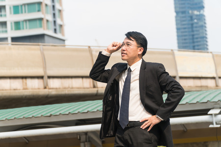 Middle-aged asian businessman holding glasses stand in modern city.Copy spaceの写真素材