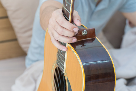 Young man holding a guitar on the bed in the bedroom.Focus hand