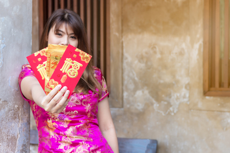 Attractive happy young woman wear cheongsam deep pink dress holding red and gold envelopes containing money for luck and prosperity family give for her. Chinese New Year celebrations conceptの写真素材