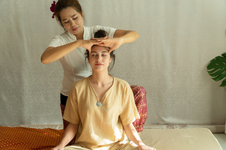 Concept thai Massage healthcare. Beautiful young woman getting herbal massage thai massage in spa salon. Attractive girl reflexology on her face with hand masseur.の写真素材
