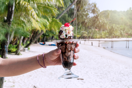 Woman hand holds cup glass ice cream chocolate sunday on summer beach in Thailand.の写真素材