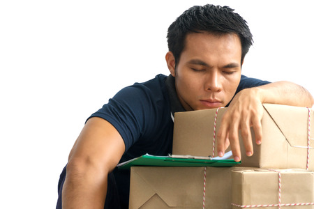 Delivery guy tired overworked sleeping on packaging boxes with clipboard. SME or freelance men sleep on cardboard box on white background.の写真素材
