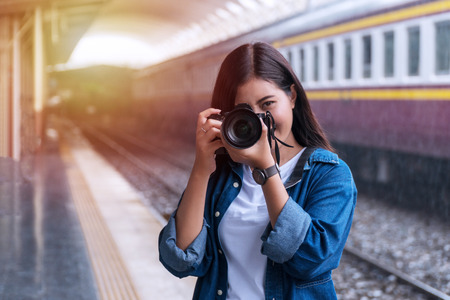 Photographer young woman taking pictures holding digital camera in station. Attractive girl travel with her camera in train station on rainy day.の写真素材