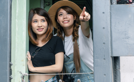 Travel and lifestyle concept. Two young woman friends watching to outside standing in the train. Traveller cheerful girl pointing at something to her friend looking at the railway station.の写真素材