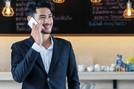 Attractive bearded talented young businessman talking mobile phones with client about new features in startup business in coffee shop.の写真素材