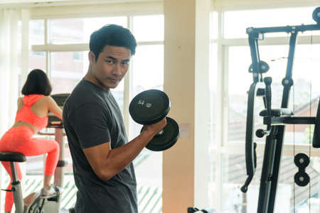 Handsome man playing with dumbbell in gym. Bodybuilder man doing heavy weight exercise with dumbbell in fitness club.の写真素材