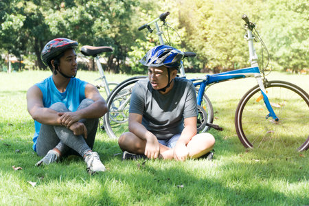 Two teenagers boy sitting on fresh grass with bicycle and holding hand in the park. Life style...