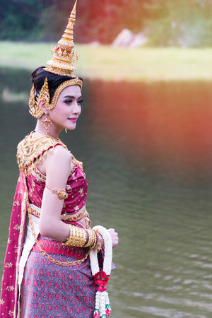 Portrait young woman wearing traditional thai purple and gold jewelry in the water park. Beautiful...