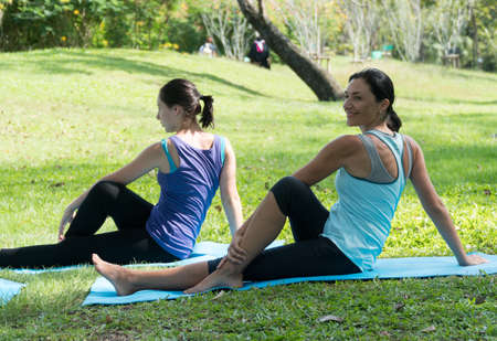 Attractive Mother and daughter Relax by doing exercise practicing yoga in the park. Healthy...