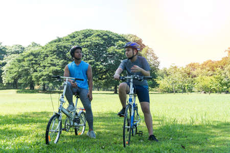 Two teenagers boy sitting on fresh grass with bicycle and holding hand in the park. Life style...