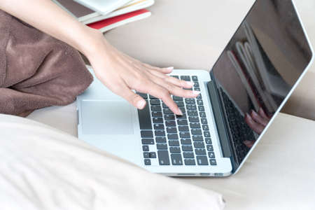 Focus hand of young woman typing on keyboard sitting on couch in the bedroom.Lifestyle concept