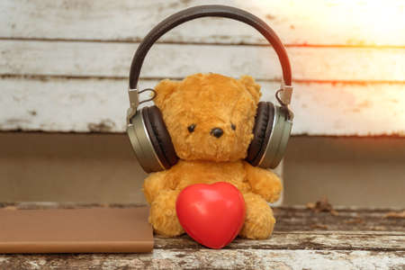 Brown teddy bear wearing headphones with red heart sitting on a chair in the garden.の写真素材