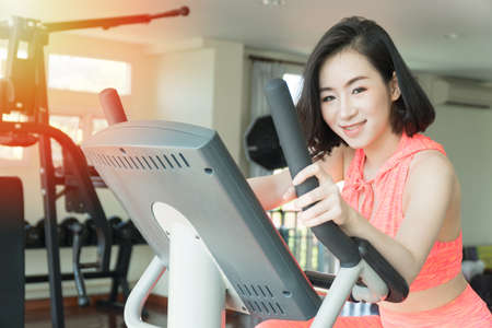Beautiful young woman slim body exercise on bicycle machine look at camera in fitness center for good healthy. Workout, sport, lifestyle concept.の写真素材