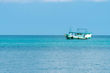Passenger boat drifts on crystal clear water near the shore line of koh kood Island, Thailand.