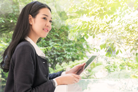 Attractive Business woman sitting hold tablet looking at something in the living room beside the garden.の写真素材