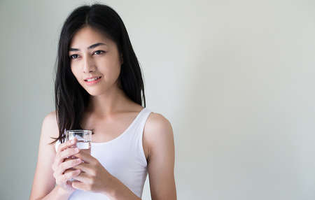Attractive young Asian woman holding glass of water in her hand on white background. Healthy concept