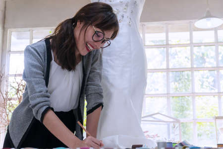 Fashion designer Asian young woman working in her studio. Attractive stylish girl wearing glasses...