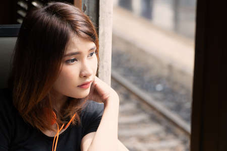 Young woman passenger sitting inside train and looking through window. Teenage girl with orange headset feels lonely and looking outside the train window.の写真素材