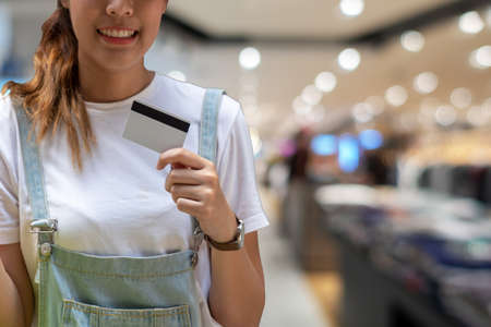 Attractive cheerful young woman holding credit card on shopping mall background. Lifestyle shopping concept.の写真素材