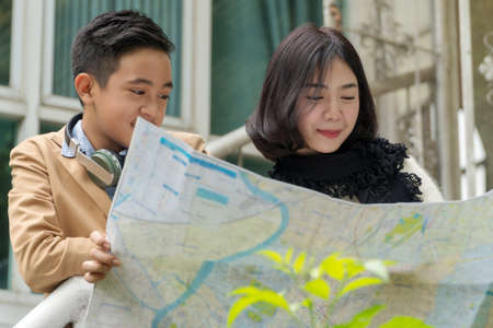 Attractive happy teenage boy and teenage girl holding map in hands and looking for their trip in holidays.の写真素材