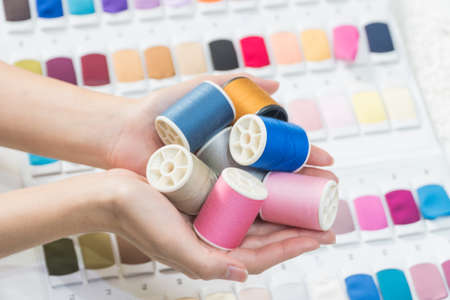 Sewing thread in the hands of colorful fabric samples background.