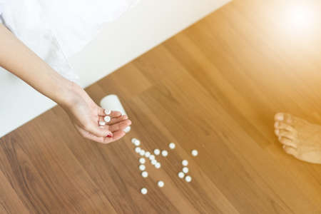 Focus hand young woman after overdosing on drugs has fallen to the floor and legs of people to come to the rescue on a wooden background.の写真素材